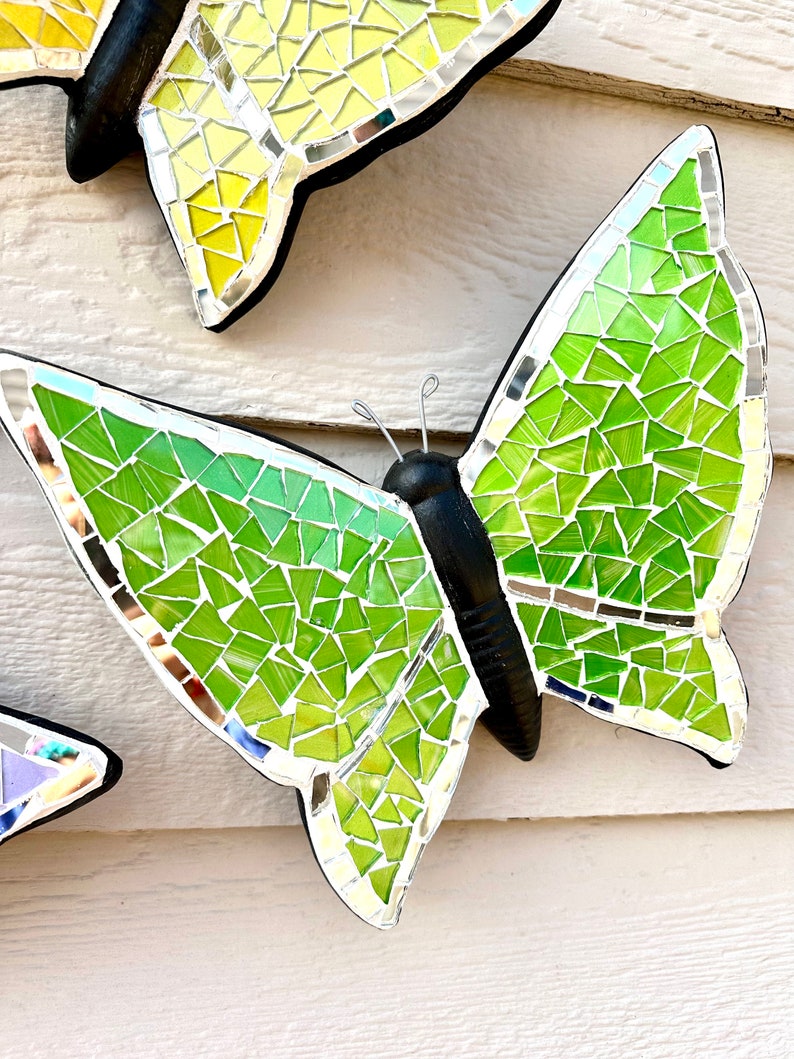 May include: A green mosaic butterfly with black wings and silver accents. The butterfly is made of small, iridescent glass tiles.