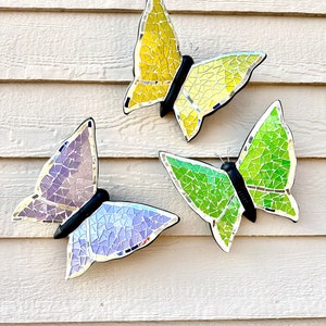May include: Three mosaic butterfly wall decorations in yellow, green, and purple. The butterflies are made of small, iridescent tiles and have a reflective finish.
