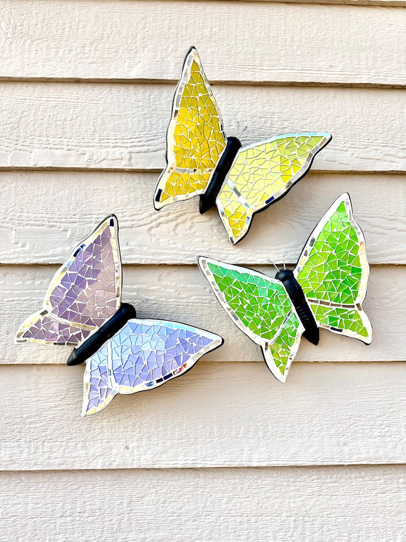 May include: Three mosaic butterfly wall decorations in yellow, green, and purple. The butterflies are made of small, iridescent tiles and have a reflective finish.