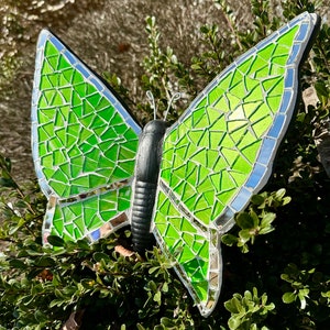 May include: A green mosaic butterfly with a black body. The butterfly is made of small, iridescent glass tiles.