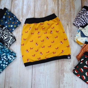 Peut inclure: Un assortiment de chutes de tissu colorées avec différents motifs, notamment des renards, des baleines et des feuilles. Les chutes de tissu sont disposées en demi-cercle sur une surface en bois.