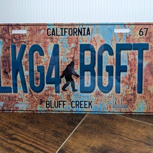May include: A rusty blue and brown metal license plate with the text "CALIFORNIA" and "BLUFF CREEK" in white. The license plate number is "LKG4 BGFT" in blue with a silhouette of Bigfoot in between the numbers.