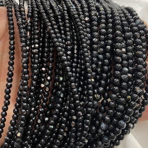 May include: A collection of strands of small, round, black beads. The beads have a glossy finish and are held in a person's hand. The beads are likely for jewelry making or crafting.