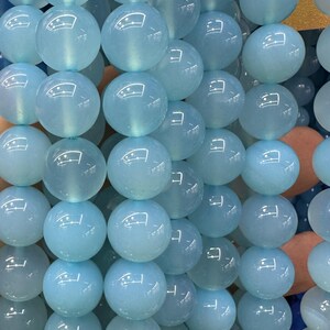 May include: Close-up of light blue, round beads. The beads are strung together, creating a textured surface. The beads have a translucent quality, reflecting light. The overall color palette is a soft, calming blue.