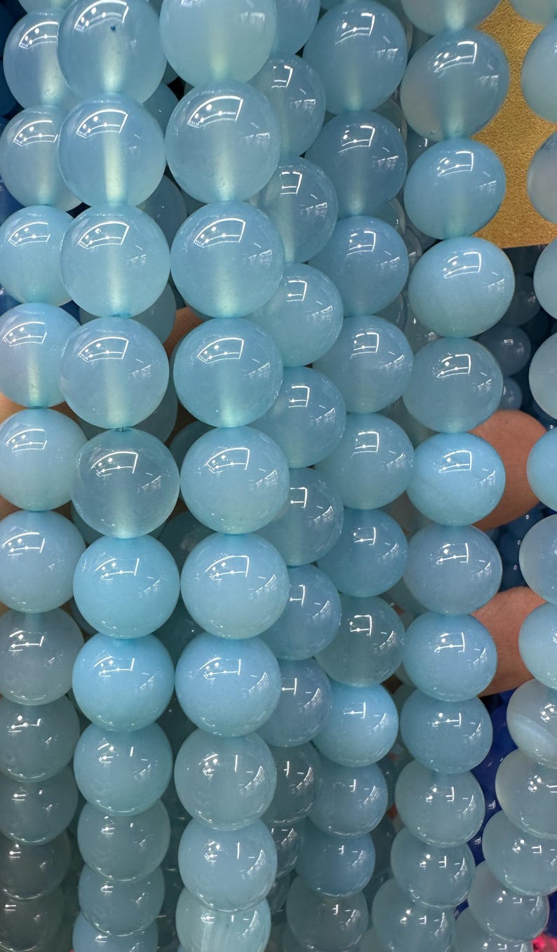 May include: Close-up of light blue, round beads. The beads are strung together, creating a textured surface. The beads have a translucent quality, reflecting light. The overall color palette is a soft, calming blue.