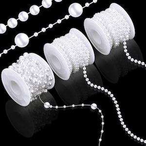 May include: White pearl bead strands and spools against a black background. The strands vary in pearl size, with some on spools and others loose. The pearls have a glossy finish, and the spools are white.