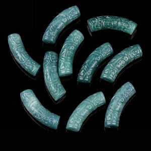 May include: A collection of teal-colored, curved beads with intricate carved designs. The beads are arranged on a black surface, showcasing their detailed patterns and smooth, polished texture. These beads are ideal for jewelry making.