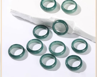 May include: A collection of ten jade rings in varying positions. The rings are a translucent teal green color and have a smooth, polished finish. The rings are round and appear to be of a uniform size, suitable for everyday wear.
