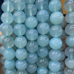 May include: Strand of light blue, translucent gemstone beads. Each round bead has a polished surface, reflecting light. The beads are strung together, creating a necklace or bracelet component. The color is a soft, calming blue.