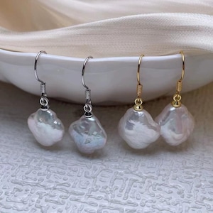 May include: Four pairs of pearl earrings. Two pairs have silver-colored hooks and two have gold-colored hooks. The pearls are white and irregularly shaped. The earrings are displayed on a white surface.