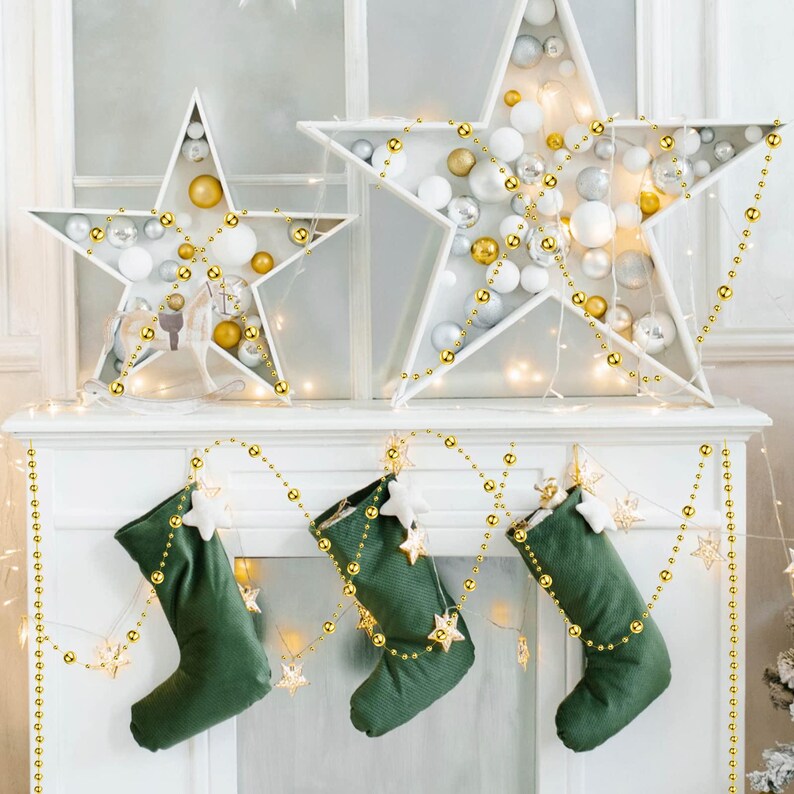 May include: A festive Christmas mantelpiece decorated with two white star-shaped ornaments filled with silver, gold, and white baubles. Three green stockings with star accents hang below, adorned with gold bead garlands.