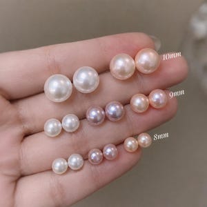 May include: A collection of spherical pearl stud earrings in white, lavender, and peach hues. The pairs are arranged by size, with labels indicating 10mm, 9mm, and 8mm diameters. Each pair features a smooth, lustrous finish and a classic round shape.