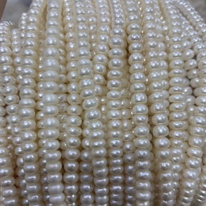 May include: Close-up of multiple strands of creamy white pearls. The pearls are uniform in size and shape, strung together to create a luxurious and elegant appearance. The strands are tightly packed, showcasing the luster and smooth texture of the pearls.