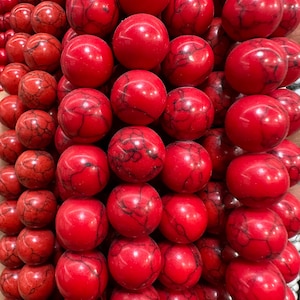 Puede incluir: Primer plano de un montón de cuentas de piedras preciosas rojas. Las cuentas son redondas y tienen un acabado liso y pulido. Están dispuestas en un patrón escalonado, creando una exhibición visualmente atractiva.