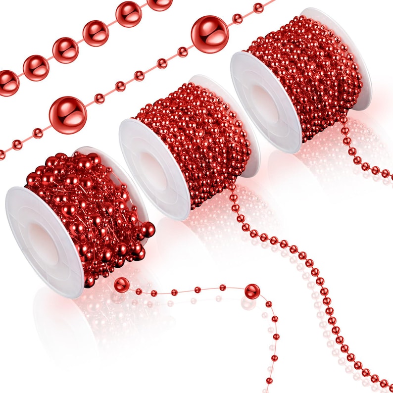 May include: Red beaded garland on white spools and loose strands. The garland features small, round beads and larger, spherical beads. The spools are arranged at different angles, showcasing the garland's texture and color. The beads have a glossy finish.