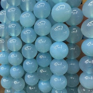 May include: Close-up of strands of light blue, round beads. The beads are smooth and have a glossy finish, reflecting light. The beads are strung together, creating a textured surface. The overall theme is jewelry making or crafting.