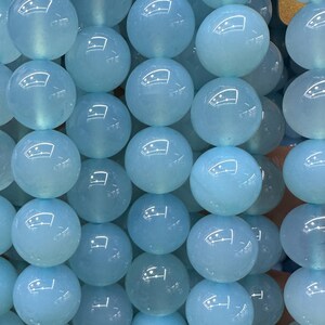 May include: Close-up of a collection of light blue, round beads. The beads have a glossy, reflective surface and appear to be strung together. The beads are a consistent size and shape, creating a uniform pattern. The overall theme is jewelry making or crafting.