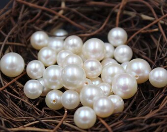 May include: A collection of off-white pearls of different sizes, resting in a bed of brown twigs. The pearls have a smooth, reflective surface, and some have small holes for stringing.
