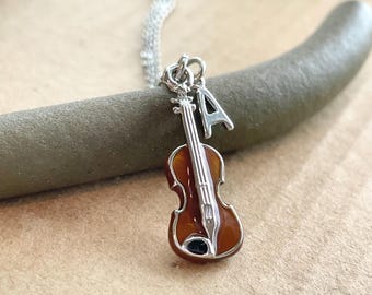 May include: A silver necklace with a brown violin charm and a silver charm with the letter 'A'.