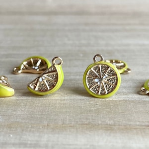 May include: Five yellow metal charms shaped like lemon slices. The charms have a gold finish and white details. The charms are perfect for adding a touch of summer to jewelry or crafts.