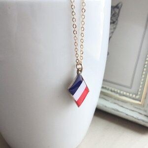 May include: A gold chain necklace with a diamond-shaped pendant featuring the French flag colors: blue, white, and red.