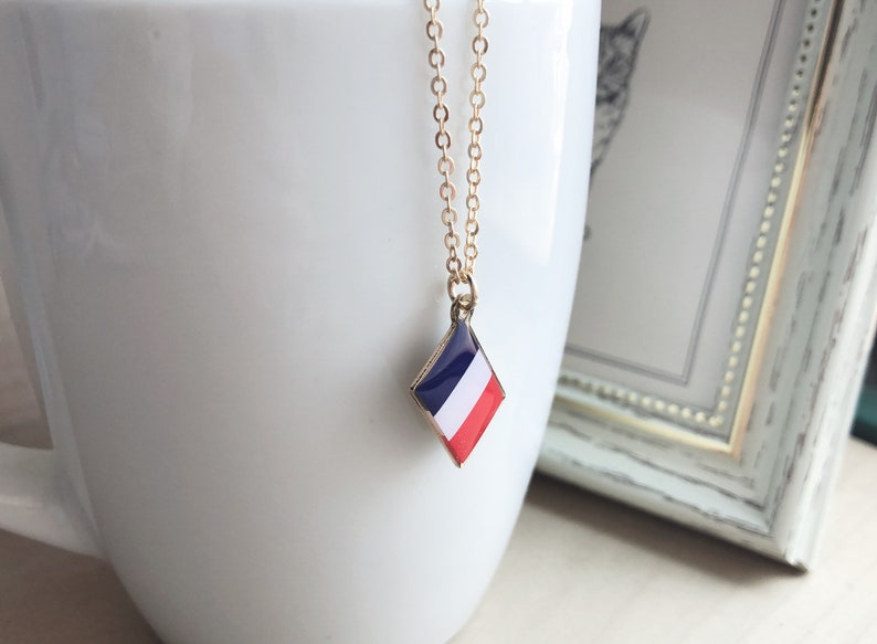 May include: A gold chain necklace with a diamond-shaped pendant featuring the French flag colors: blue, white, and red.