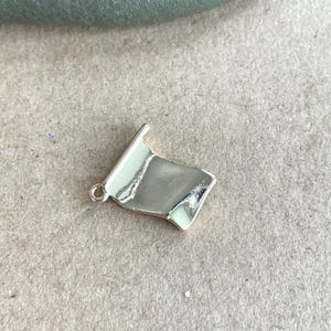 May include: A gold-colored metal charm shaped like a flag, with a slightly curved surface.