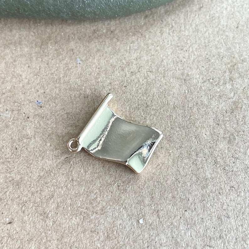 May include: A gold-colored metal charm shaped like a flag, with a slightly curved surface.