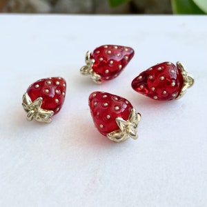 May include: Four red glass strawberry buttons with gold accents. The strawberries have a dotted texture and gold leaf accents.