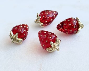 May include: Four red glass strawberry buttons with gold accents. The strawberries have a dotted texture and gold leaf accents.