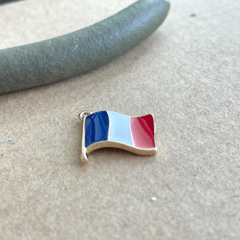 May include: A gold-colored charm in the shape of a French flag. The flag is blue, white, and red.