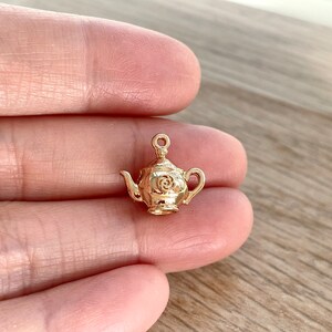 Pu&ograve; includere: Un ciondolo a forma di teiera dorata con un design floreale. Il ciondolo &egrave; piccolo e dettagliato, perfetto per aggiungere un tocco di fantasia a gioielli o artigianato.