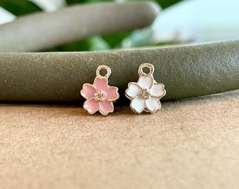 May include: Two small metal flower charms, one pink and one white, with a five-petal design. The charms are perfect for adding a touch of whimsy to jewelry or crafts.