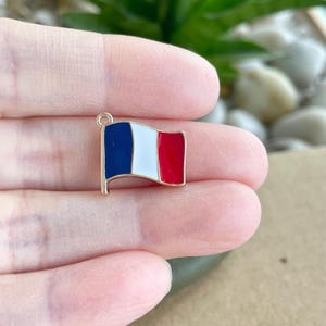 May include: Gold-toned charm featuring a French flag design. The flag is blue, white, and red with a gold-toned loop at the top.