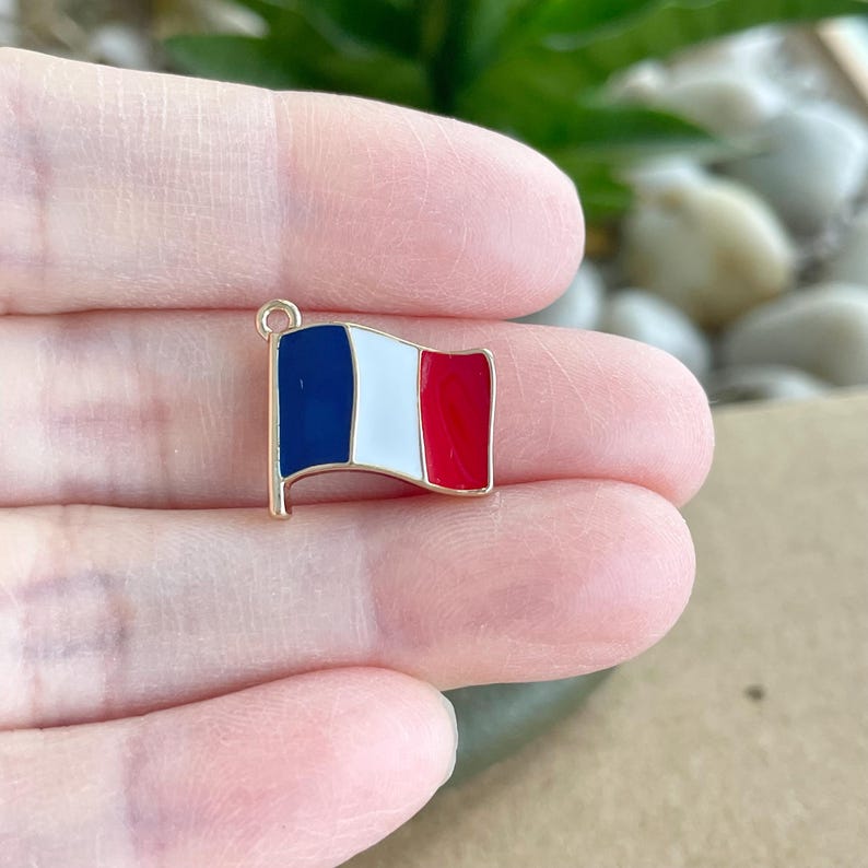 May include: Gold-toned charm featuring a French flag design. The flag is blue, white, and red with a gold-toned loop at the top.