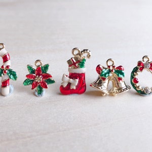 May include: Six gold-tone Christmas charm pendants with red and green enamel. The charms include a candy cane, a poinsettia, a stocking, two bells, and a wreath.