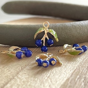 May include: Four gold-tone charms featuring blue enamel berries and green enamel leaves. The charms are ideal for jewellery making or adding a touch of whimsy to crafts.