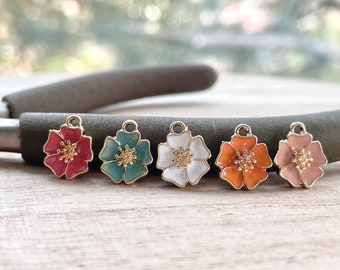 May include: Five gold flower charms with enamel paint in different colors: pink, teal, white, orange, and light pink. The charms have a loop at the top for attaching to jewelry.