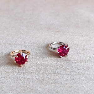 May include: Two rings with red gemstone settings. The ring on the left has a gold band and the ring on the right has a silver band.