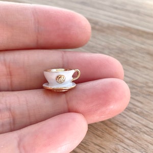 Pu&ograve; includere: Una minuscola tazzina da t&egrave; bianca e un piattino con bordi dorati. La tazza ha un accento dorato sul davanti.