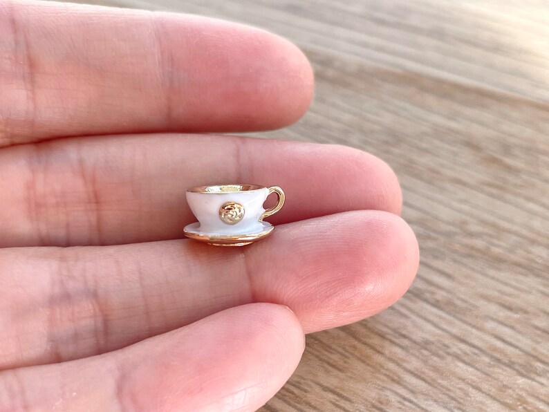 Pu&ograve; includere: Una minuscola tazzina da t&egrave; bianca e un piattino con bordi dorati. La tazza ha un accento dorato sul davanti.