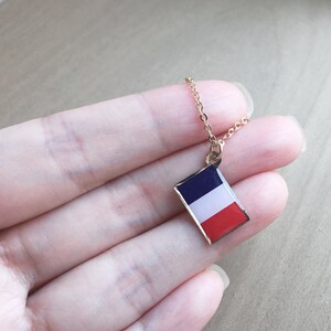 May include: A gold chain necklace with a small pendant featuring the French flag. The pendant is rectangular and has the colors blue, white, and red.