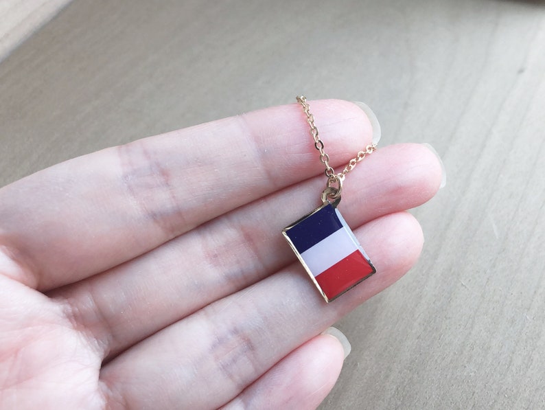May include: A gold chain necklace with a small pendant featuring the French flag. The pendant is rectangular and has the colors blue, white, and red.