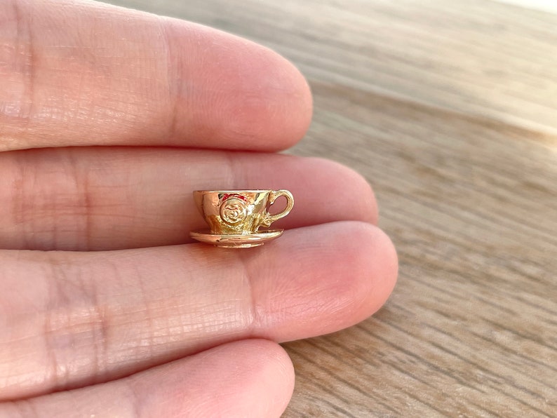 Pu&ograve; includere: Un piccolo ciondolo a forma di tazzina da t&egrave; e piattino dorato. La tazzina da t&egrave; ha un design in rilievo sul lato.