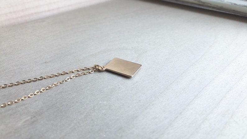 May include: A gold chain necklace with a small, rectangular pendant.