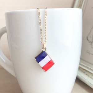 May include: A gold chain necklace with a diamond-shaped pendant featuring the French flag colors: blue, white, and red.