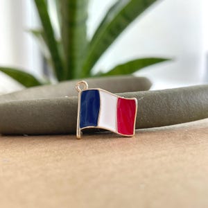 May include: A gold-colored charm in the shape of a French flag. The flag is blue, white, and red.