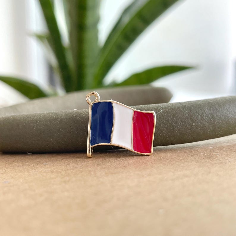 May include: A gold-colored charm in the shape of a French flag. The flag is blue, white, and red.