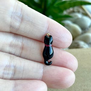 May include: Black enamel cat charm with a red collar. The charm has a gold loop for attaching to a necklace or bracelet.