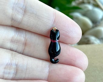 May include: Black enamel cat charm with a red collar. The charm has a gold loop for attaching to a necklace or bracelet.